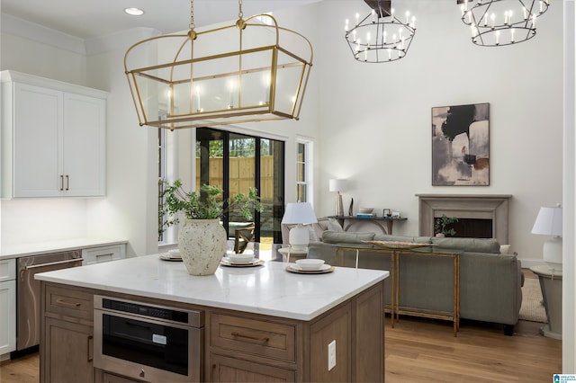 kitchen featuring light wood-type flooring, a kitchen island, a notable chandelier, and stainless steel dishwasher