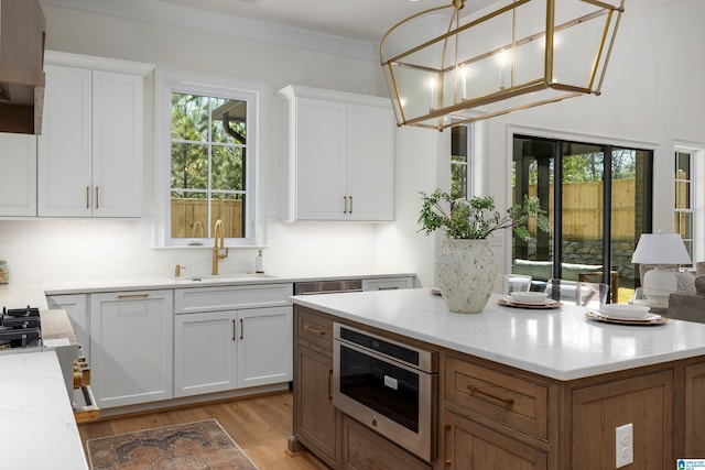 kitchen with white cabinetry, light wood-style flooring, light stone countertops, and a sink