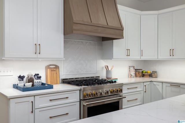 kitchen featuring high end stainless steel range, tasteful backsplash, white cabinetry, light stone countertops, and custom exhaust hood