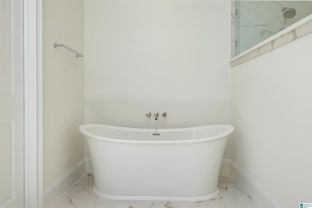 bathroom featuring marble finish floor, a freestanding bath, a shower, and baseboards