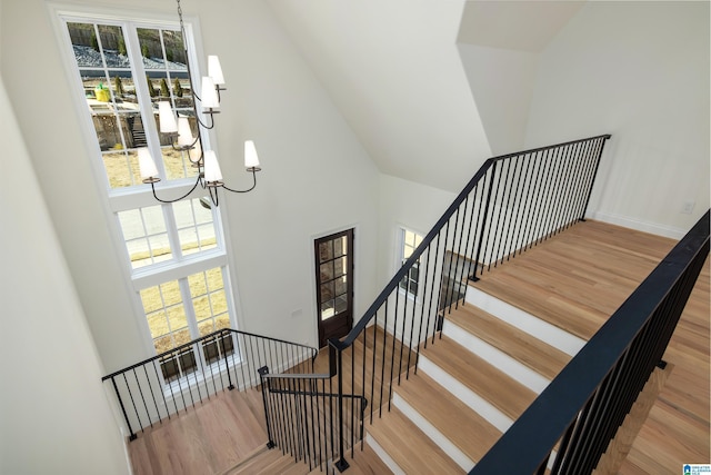 staircase featuring baseboards, a notable chandelier, a high ceiling, and wood finished floors