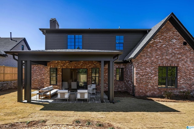 rear view of house featuring fence, a yard, a chimney, a patio area, and brick siding