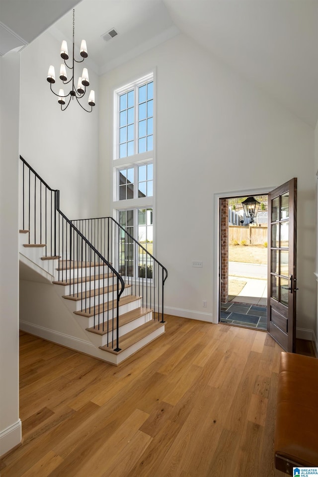 entrance foyer featuring wood finished floors, visible vents, high vaulted ceiling, stairs, and a chandelier