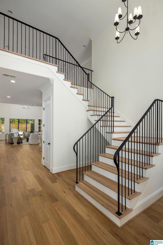 staircase with visible vents, baseboards, a chandelier, a towering ceiling, and wood finished floors