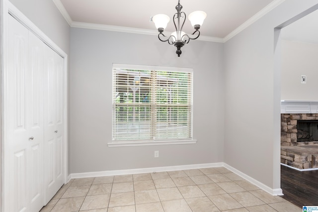 unfurnished dining area featuring a stone fireplace, ornamental molding, light tile patterned flooring, and a notable chandelier