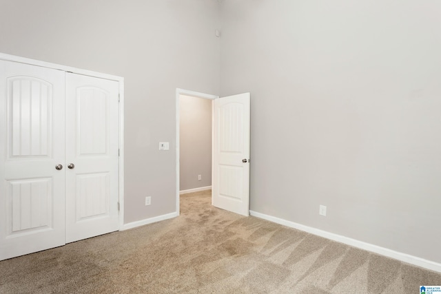 unfurnished bedroom featuring a high ceiling, a closet, and light colored carpet