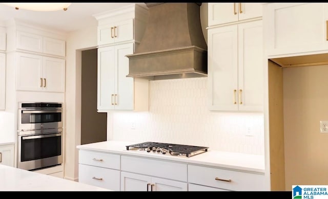 kitchen with white cabinetry, custom range hood, stainless steel appliances, and backsplash