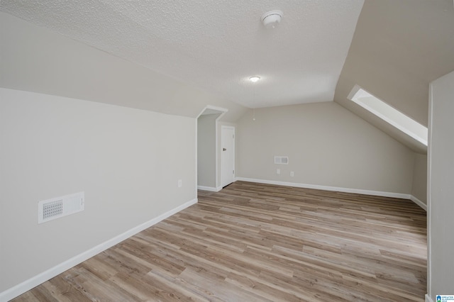 additional living space featuring vaulted ceiling with skylight, a textured ceiling, and light wood-type flooring