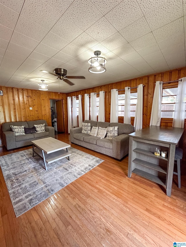 living room with ceiling fan, wooden walls, and light wood-type flooring