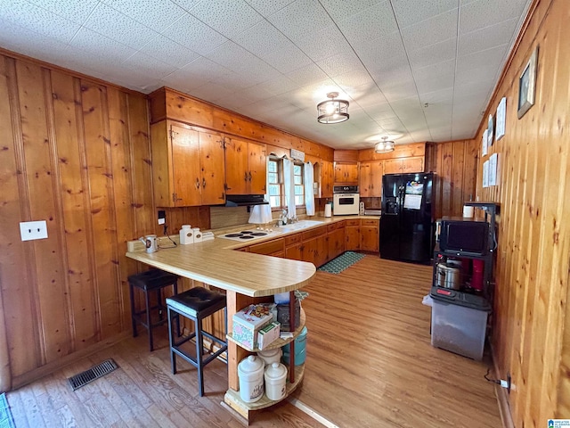 kitchen with white appliances, wooden walls, light hardwood / wood-style flooring, and kitchen peninsula