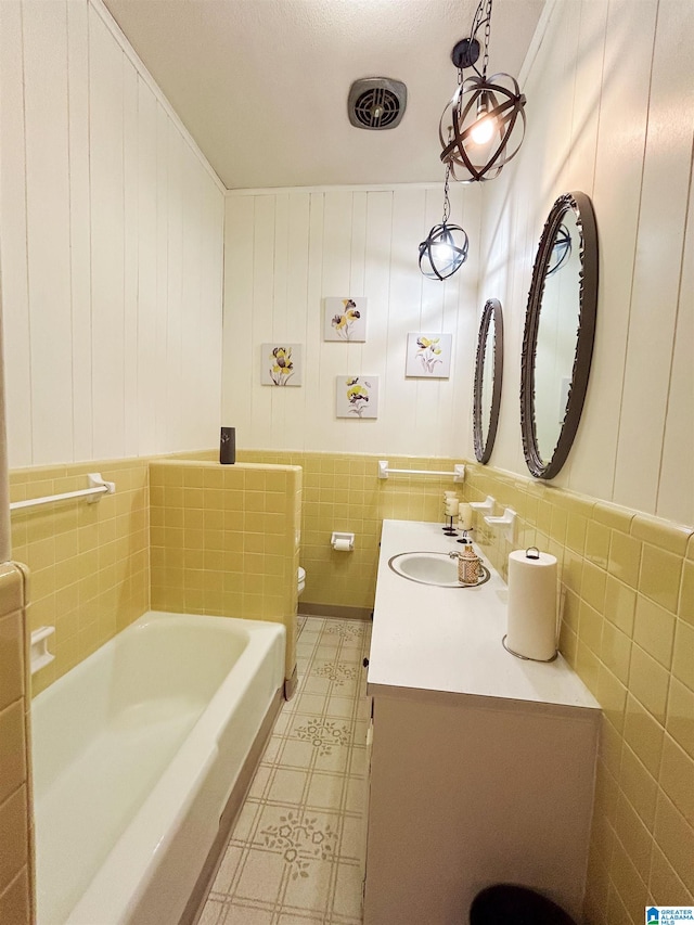 bathroom with tile walls, a tub to relax in, vanity, and toilet