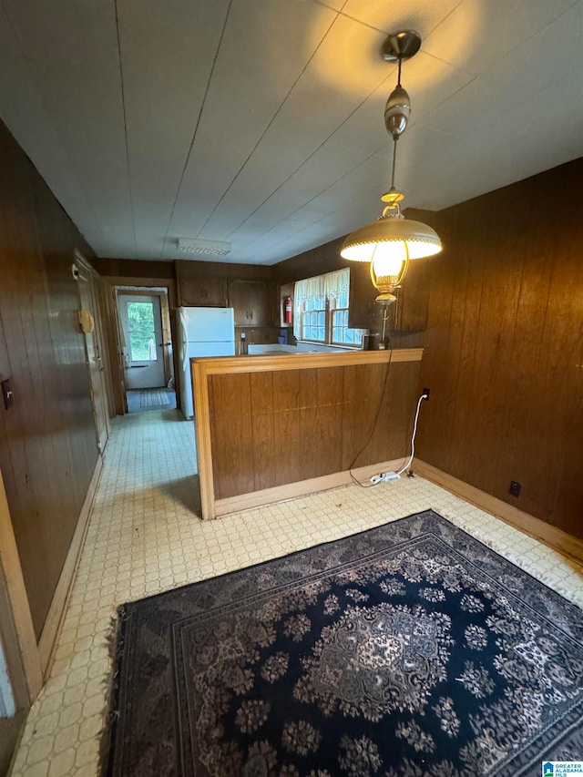 interior space featuring kitchen peninsula, wood walls, and white refrigerator