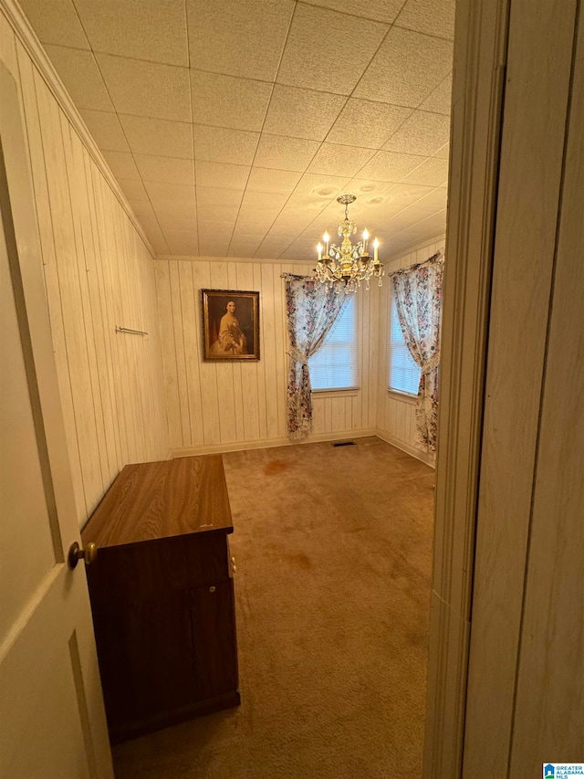 interior space with carpet floors, wooden walls, and a chandelier