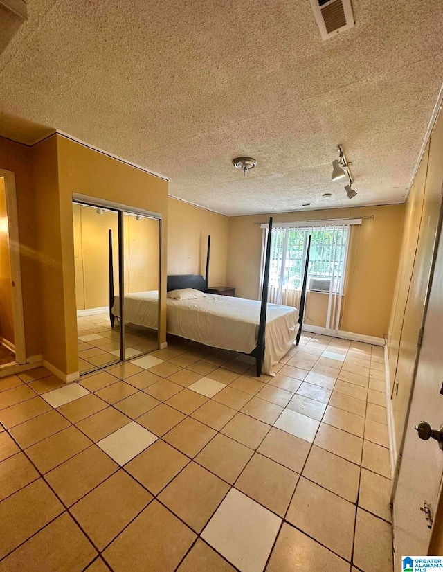 unfurnished bedroom with a closet, a textured ceiling, rail lighting, light tile patterned floors, and ornamental molding