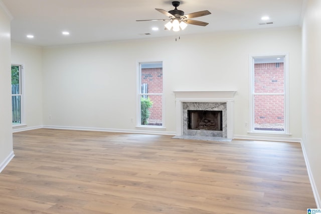 unfurnished living room with a wealth of natural light, a high end fireplace, light hardwood / wood-style floors, and ceiling fan