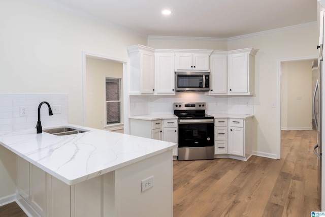 kitchen with kitchen peninsula, appliances with stainless steel finishes, light stone countertops, sink, and white cabinets