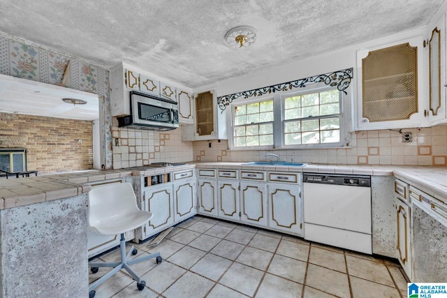 kitchen featuring tasteful backsplash, light tile patterned floors, stainless steel appliances, tile counters, and sink