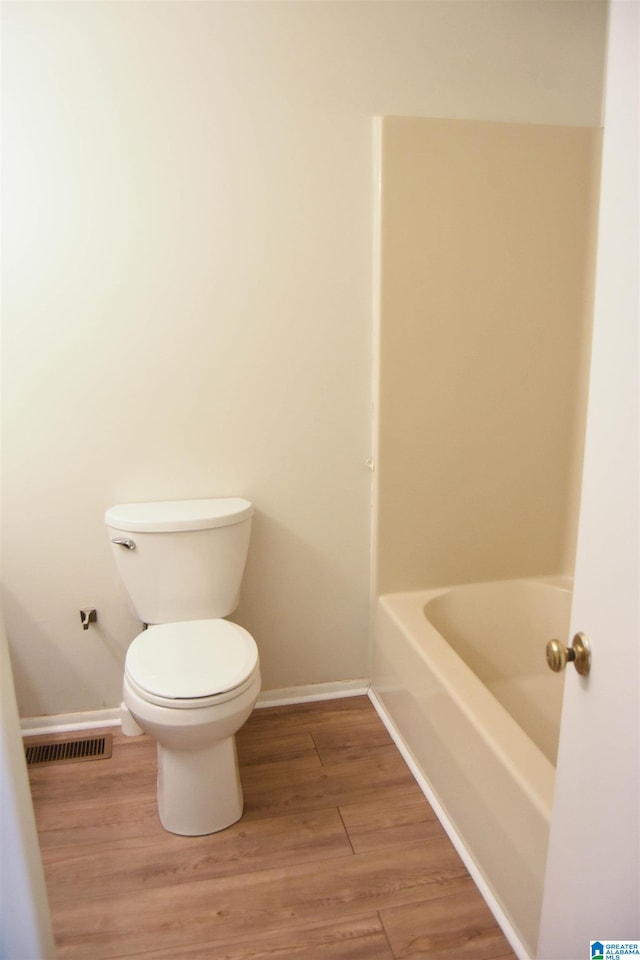 bathroom with a tub to relax in, hardwood / wood-style floors, and toilet