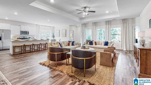 living room featuring light wood-type flooring, a tray ceiling, a wealth of natural light, and ceiling fan