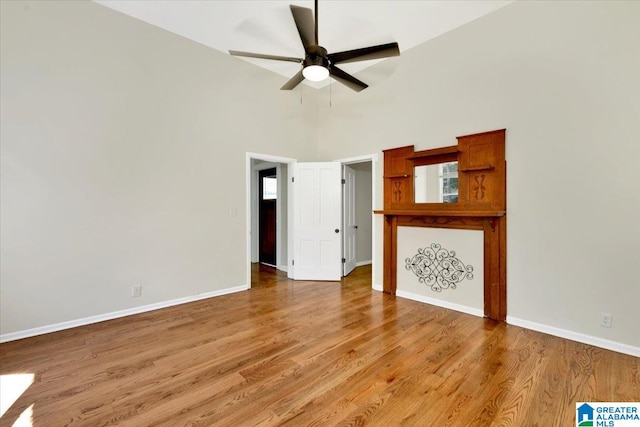 unfurnished living room featuring light wood-type flooring, a towering ceiling, and ceiling fan