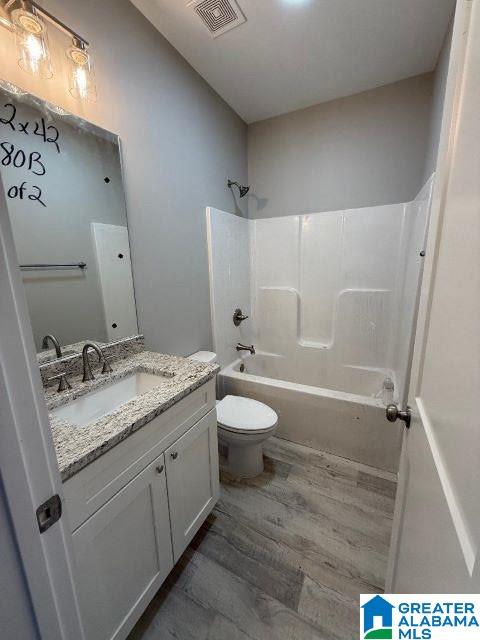 bathroom featuring visible vents, toilet, vanity, wood finished floors, and shower / bathtub combination