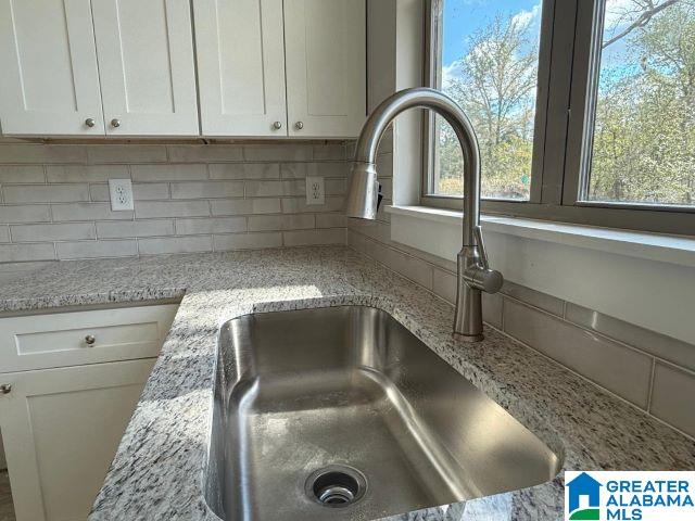 room details featuring a sink, light stone counters, white cabinets, and backsplash