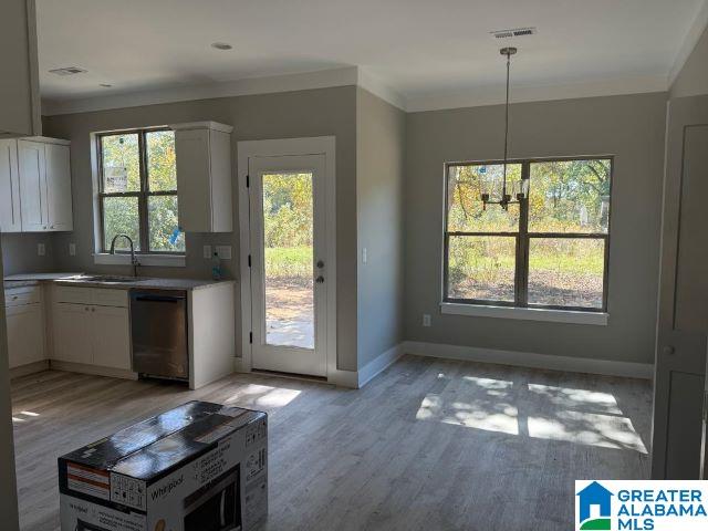 interior space with a sink, hanging light fixtures, light countertops, white cabinetry, and dishwasher