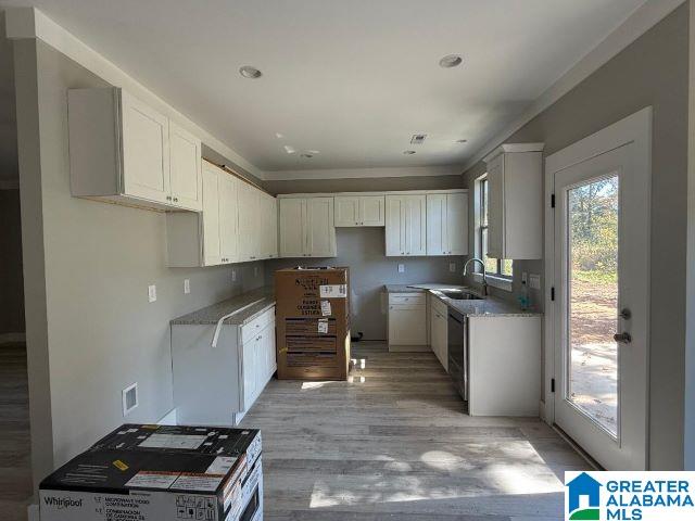 kitchen with light wood finished floors, white cabinetry, and a sink