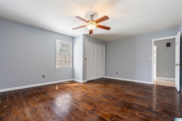 unfurnished bedroom with a textured ceiling, ceiling fan, dark wood-type flooring, and a closet