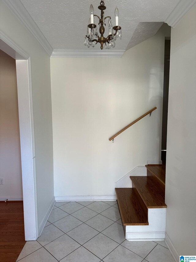 staircase with a textured ceiling, ornamental molding, tile patterned floors, a notable chandelier, and baseboards