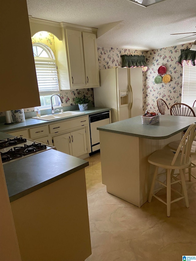 kitchen with a textured ceiling, sink, a kitchen breakfast bar, white appliances, and cream cabinets