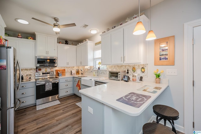 kitchen with appliances with stainless steel finishes, kitchen peninsula, pendant lighting, and white cabinets