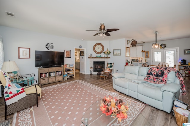 living room featuring ceiling fan, hardwood / wood-style floors, and a tile fireplace