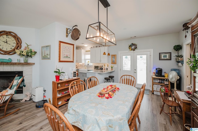 dining space featuring french doors, an inviting chandelier, light wood-type flooring, and a tiled fireplace