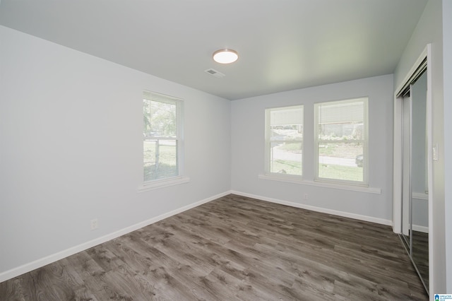 unfurnished bedroom featuring multiple windows, dark wood-type flooring, and a closet