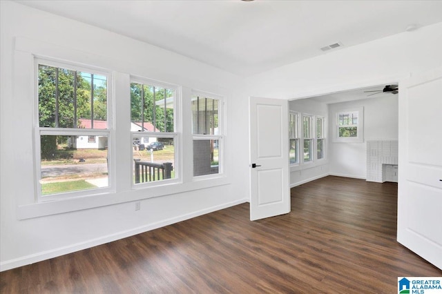 unfurnished room featuring a fireplace, dark hardwood / wood-style floors, ceiling fan, and plenty of natural light