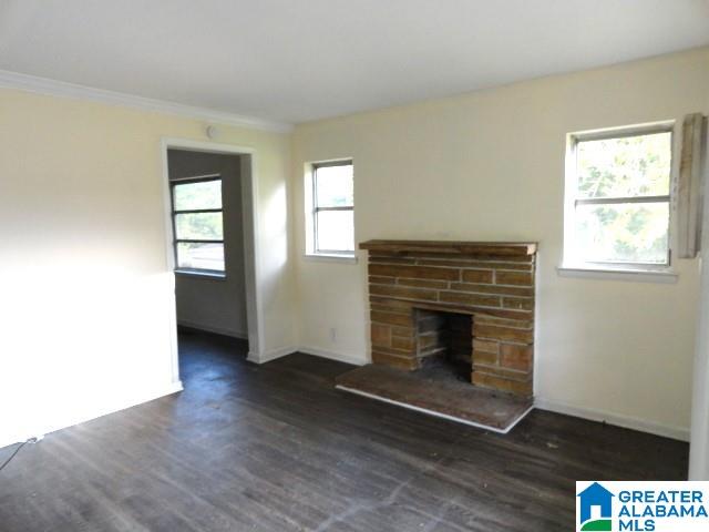 unfurnished living room featuring a stone fireplace, dark hardwood / wood-style flooring, and a healthy amount of sunlight