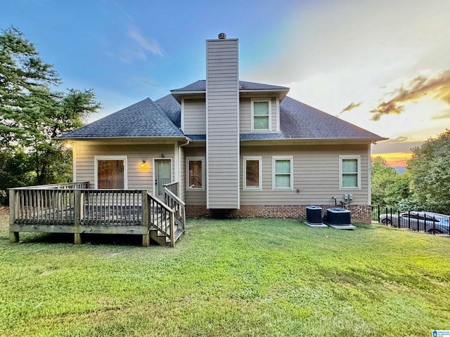 back house at dusk with a wooden deck and a lawn