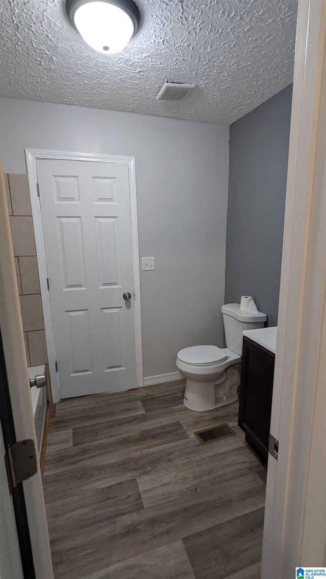 bathroom with a textured ceiling, hardwood / wood-style flooring, a washtub, vanity, and toilet