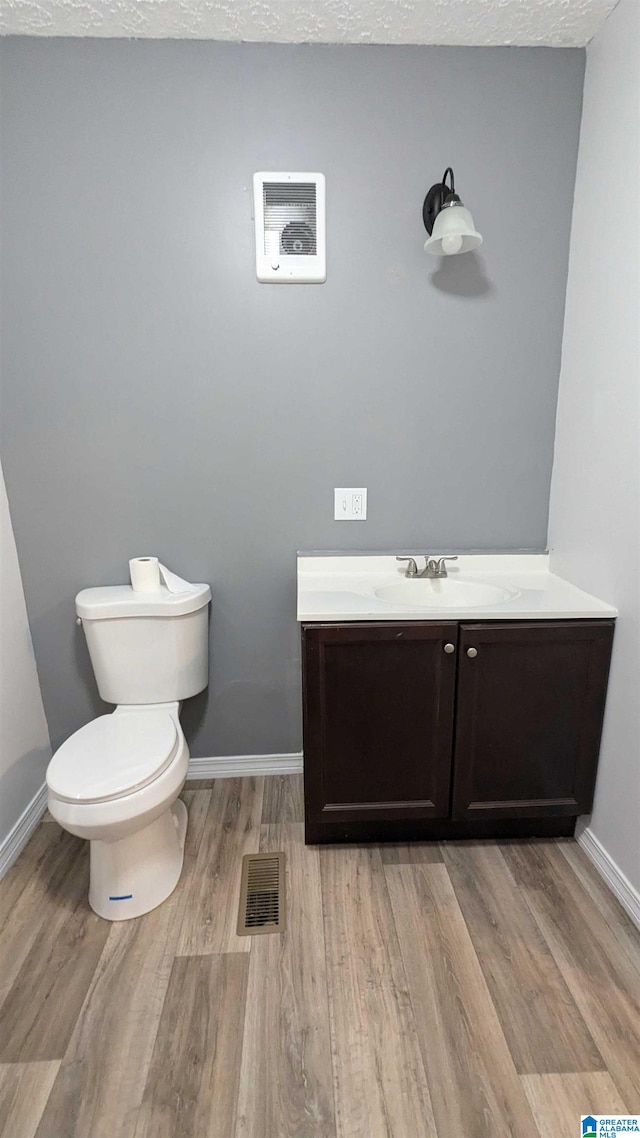 bathroom with a textured ceiling, wood-type flooring, vanity, and toilet