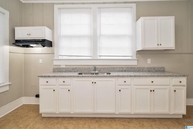 kitchen with light tile patterned flooring, sink, light stone counters, and white cabinets