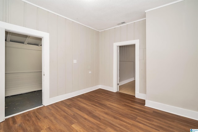 unfurnished bedroom with a closet, a textured ceiling, dark hardwood / wood-style floors, wooden walls, and crown molding