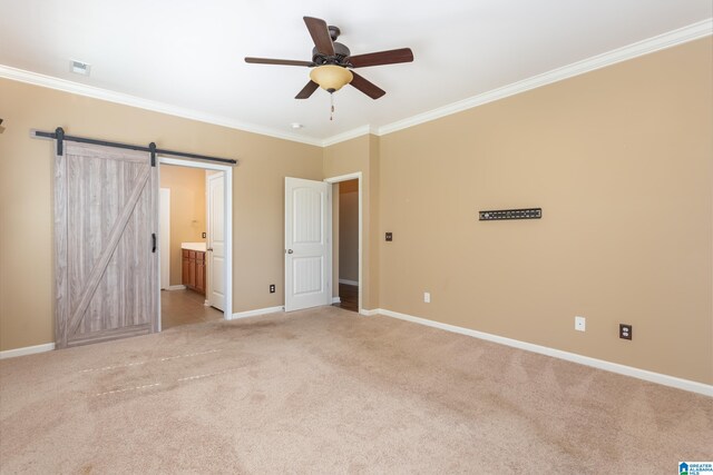 unfurnished bedroom with a barn door, ceiling fan, ensuite bathroom, ornamental molding, and light carpet