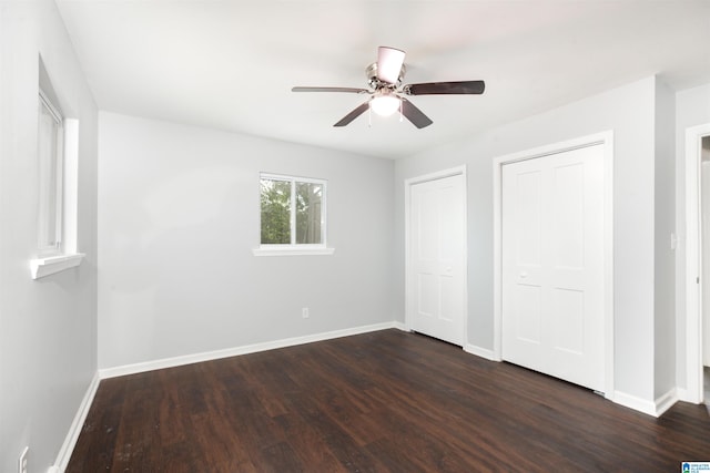 unfurnished bedroom with ceiling fan, two closets, and dark wood-type flooring