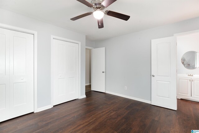 unfurnished bedroom with two closets, ceiling fan, ensuite bath, and dark hardwood / wood-style flooring