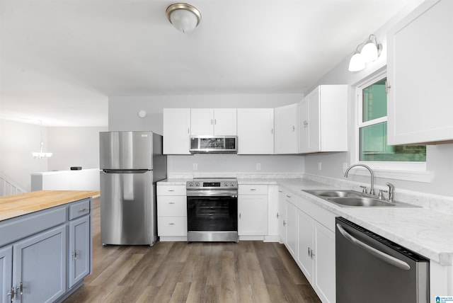 kitchen featuring appliances with stainless steel finishes, hanging light fixtures, white cabinets, dark hardwood / wood-style flooring, and sink