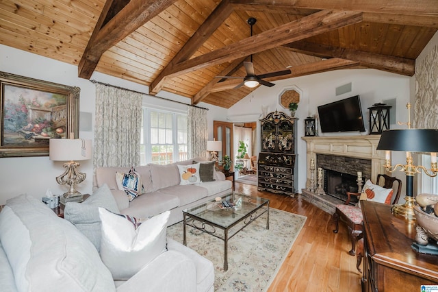 living room with wood ceiling, a stone fireplace, light wood-type flooring, ceiling fan, and vaulted ceiling with beams