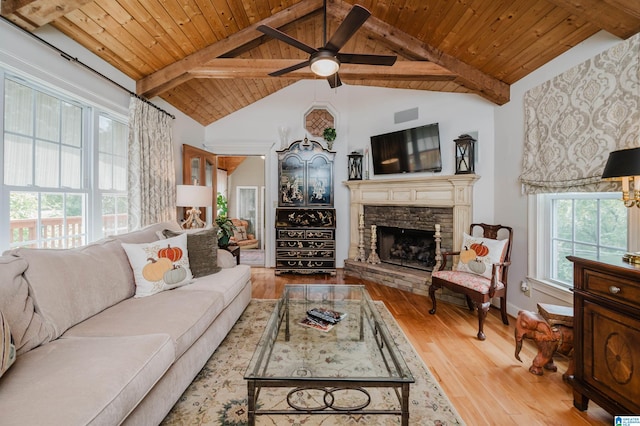 living room with wood-type flooring, a wealth of natural light, ceiling fan, and a stone fireplace