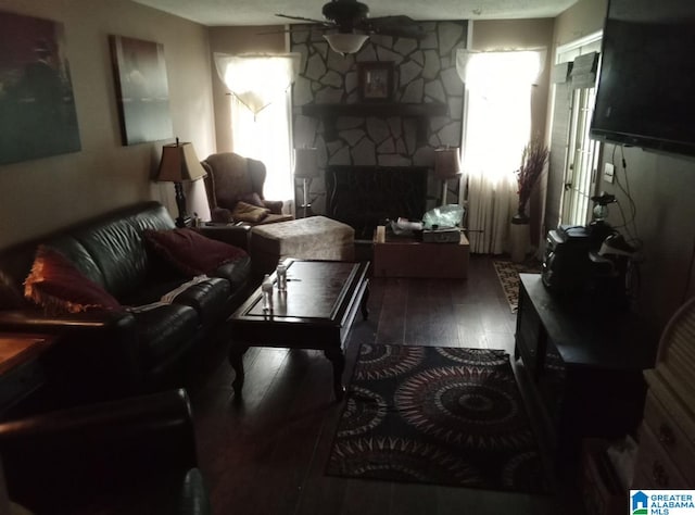 living room with a stone fireplace, dark hardwood / wood-style flooring, and ceiling fan