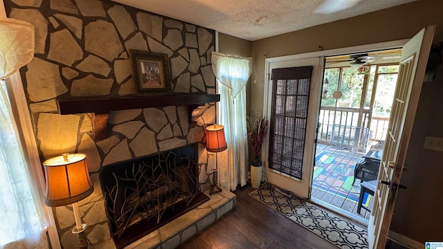 living room with a textured ceiling, wood-type flooring, a stone fireplace, and ceiling fan